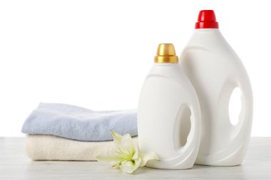 Kumaş yumuşatıcı şişeler, üst üste dizilmiş elbiseler ve çiçek beyaz arka plana karşı ahşap masa