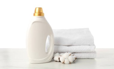 Bir şişe yumuşatıcı, beyaz arkaplana karşı mermer masada istiflenmiş havlular ve pamuk çiçekleri.