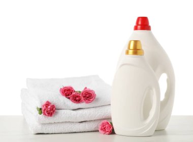 Kumaş yumuşatıcı şişeler, beyaz arkaplana karşı mermer masaya yığılmış havlular ve çiçekler.