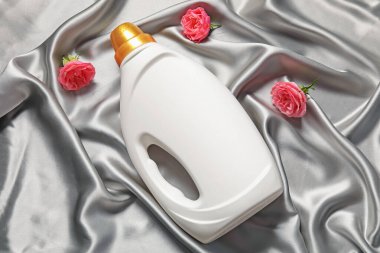 Bir şişe yumuşatıcı ve gri kumaş üzerinde çiçekler, düz yatıyordu.