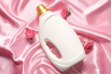 Bir şişe yumuşatıcı ve pembe kumaş üzerinde çiçekler.