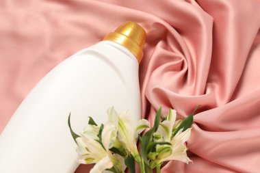 Bir şişe yumuşatıcı ve pembe kumaş üzerinde çiçekler.