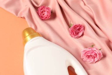 Bir şişe yumuşatıcı, çiçekler ve pembe kumaş mercan arka planda, üst tarafta.