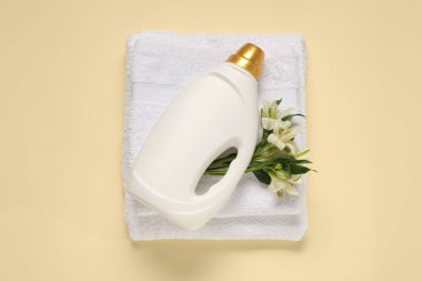 Bir şişe yumuşatıcı, çiçekler ve bej arka planda terry havlular.
