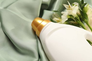 Bir şişe yumuşatıcı ve yeşil kumaş üzerinde çiçekler.