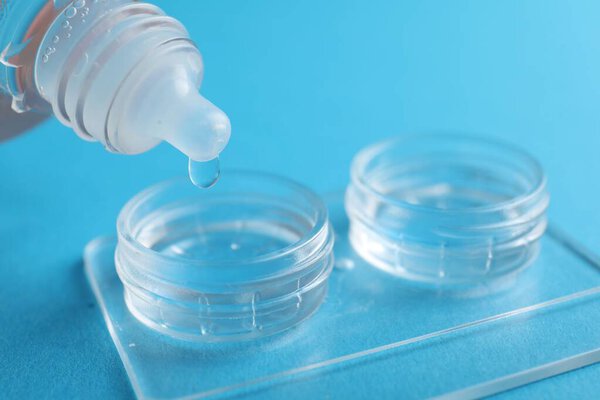 Dripping solution into case with contact lenses on light blue background, closeup