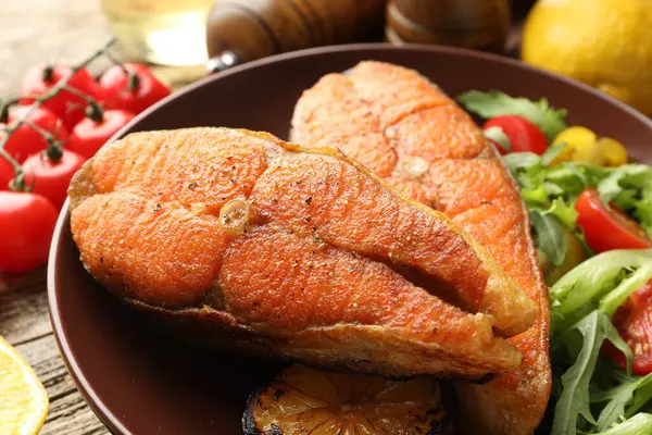 Deniz ürünleri. Ahşap masada salata ile servis edilen lezzetli somon biftekleri, yakın plan.