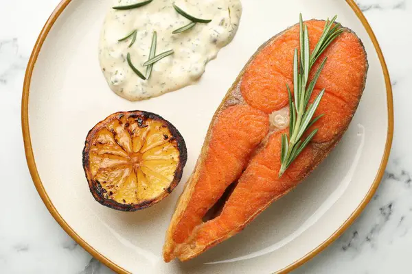 Deniz ürünleri. Sos, biberiye ve limon ile servis edilen lezzetli somon bifteği, beyaz mermer masa, üst manzara.