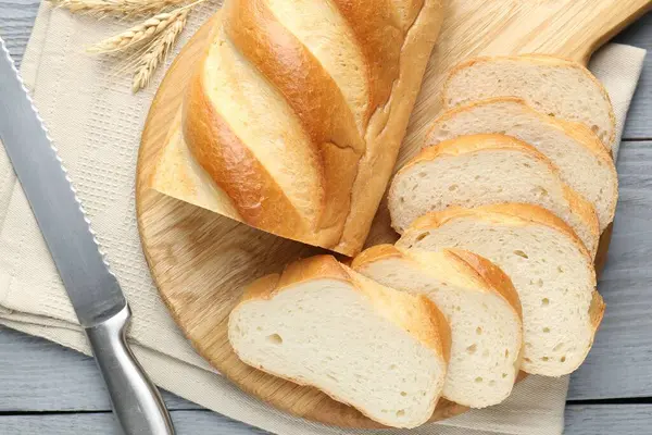 Dilimlenmiş ekmek ve bıçak gri ahşap masada, düz yatıyordu.