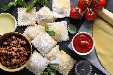 Pişmemiş ravioli, bolonez, sos, domates ve fesleğen siyah masada, düz yatıyordu.