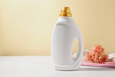 Bir şişe yumuşatıcı, temiz kıyafetler ve karanfil çiçekleri açık sarı arka planda beyaz ahşap masa üzerinde. Metin için boşluk