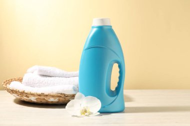 Bir şişe yumuşatıcı, terry havlular ve beyaz ahşap masada açık sarı arka plana karşı orkide çiçeği.