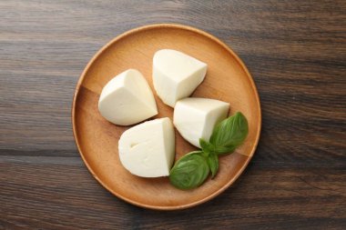 Ahşap masanın üstünde lezzetli mozzarella peyniri ve fesleğen parçaları.