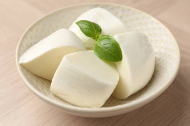 Nefis mozzarella peyniri ve fesleğen parçaları ahşap masada, yakın plan.