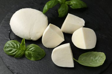 Lezzetli mozzarella peyniri ve fesleğen parçaları karanlık masada, yakın plan.