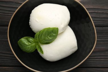 Lezzetli mozzarella peyniri ve fesleğen parçaları ahşap masada, üst tarafta.