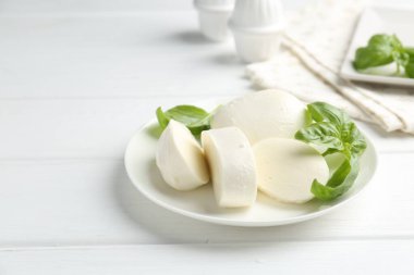 Beyaz ahşap masada lezzetli mozzarella peyniri ve fesleğen parçaları. Metin için boşluk