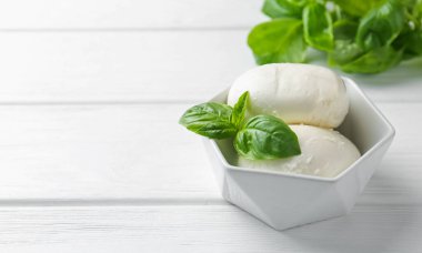 Lezzetli mozzarella peyniri ve fesleğen parçaları beyaz ahşap masada, yakın plan. Metin için boşluk