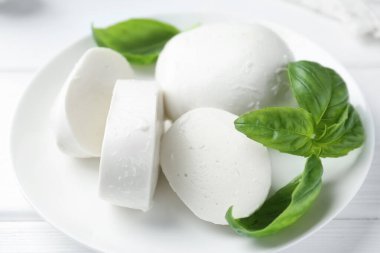 Lezzetli mozzarella peyniri ve fesleğen parçaları beyaz ahşap masada, yakın plan.
