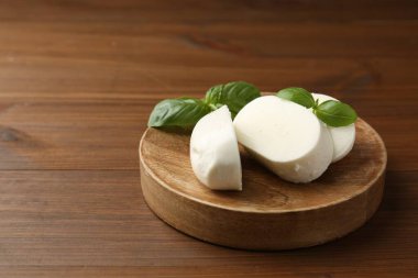 Lezzetli mozzarella peyniri parçaları ve fesleğen yaprakları ahşap masada, yakın plan. Metin için boşluk