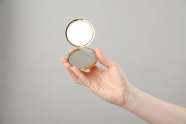 Gri arka planda açık cep aynası tutan kadın, yakın plan.