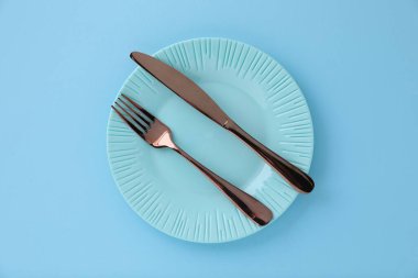 Açık mavi zemin üzerinde boş tabak ve çatal bıçak takımı, üst görünüm