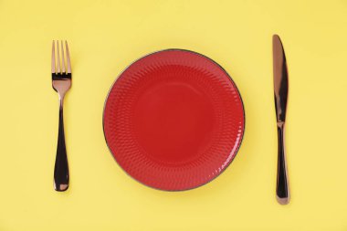 Sarı arka planda boş tabak ve çatal bıçak takımı, üst görünümde.