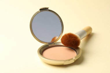 Aynalı yüz pudrasını aç ve bej arkaplanda fırçala, yakın plan