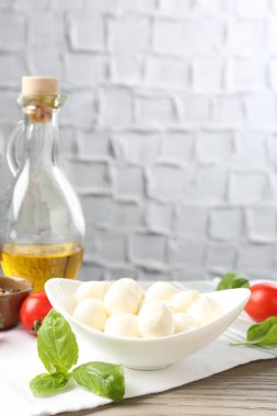 Lezzetli mozzarella peyniri topları, domatesler, fesleğen ve yağ ahşap masada, yakın plan.