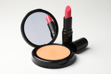 Aynalı açık yüz pudrası ve açık gri arkaplanda ruj, yakın plan.