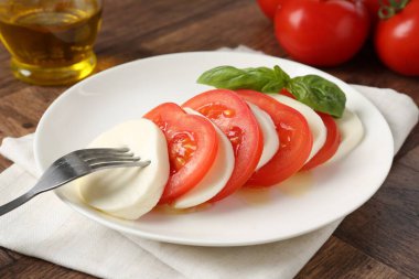 Lezzetli mozzarella, domates, yağ ve fesleğen ahşap masada, yakın plan.