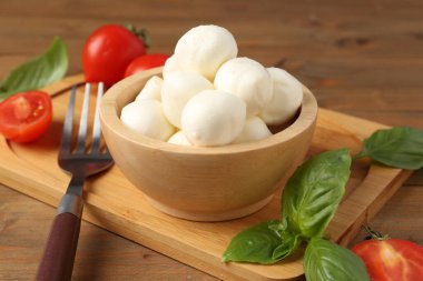 Lezzetli mozarella topları, domatesler ve fesleğenler ahşap masada, yakın plan.