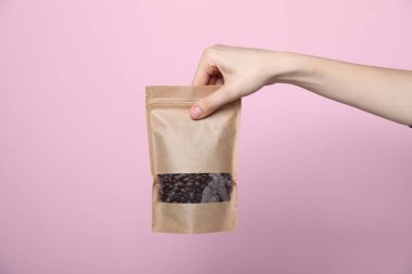 Elinde pembe arka planda kahve çekirdekleri olan fermuarlı stand-up çantası tutan kadın, yakın plan. Tasarım için model