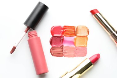 Beyaz arka planda renkli dudak parlatıcıları ve rujlar, düz bir zemin.
