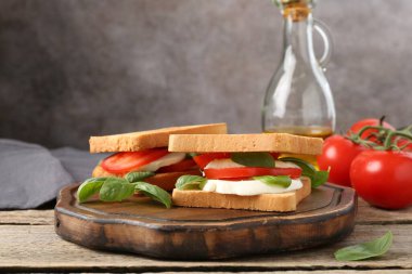 Mozarella peynirli, domatesli ve ahşap masadaki fesleğenli lezzetli sandviçler.