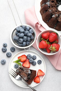 Açık gri desenli masada çilekli, nane ve yaban mersinli leziz çikolatalı kek.