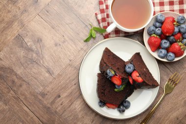Tahta masada servis edilen çilekli ve yaban mersinli çikolatalı kek parçaları. Metin için boşluk