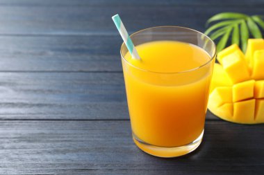 Bardakta lezzetli mango suyu, taze meyve ve ahşap masada yeşil yapraklar, yakın plan. Metin için boşluk