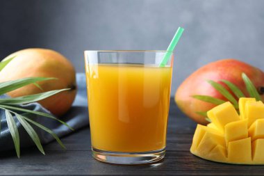 Bardakta lezzetli mango suyu, taze meyve ve ahşap masada yeşil yapraklar, yakın plan.