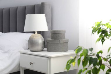 Yatağın yanında lamba ve dekor olan bir komodin.