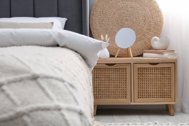 Yatağın yanında ayna, dekor ve kitap olan bir komodin.