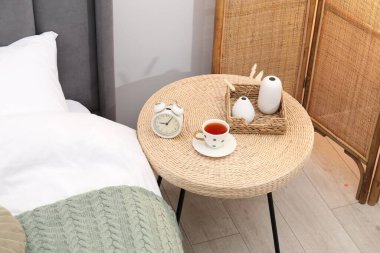 Çalar saati olan yan masa, yatağın yanında bir fincan çay ve dekor, manzaranın üstünde.