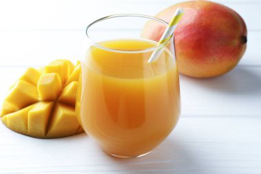 Bardakta lezzetli mango suyu ve beyaz ahşap masada taze meyveler, yakın plan.