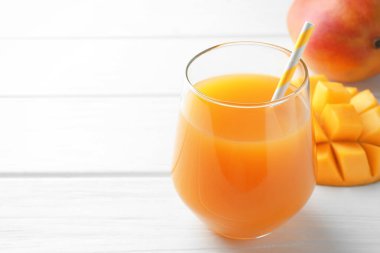 Bardakta lezzetli mango suyu ve beyaz ahşap masada taze meyveler, yakın plan. Metin için boşluk