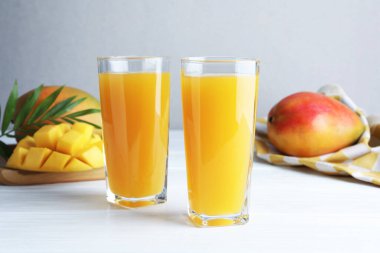 Bardakta lezzetli mango suyu, taze meyve ve beyaz ahşap masada yeşil yapraklar.