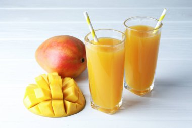 Bardakta lezzetli mango suyu ve beyaz ahşap masada taze meyve, yakın plan.