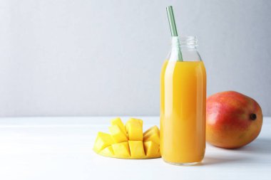 Cam şişede lezzetli mango suyu ve beyaz ahşap masada taze meyve, mesaj için yer var.