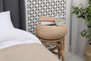 Çalar saati olan yan masa ve yatağın yanında kitaplar.