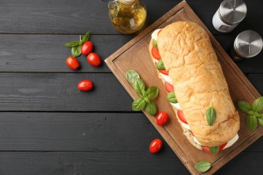 Mozarella peynirli, domatesli, fesleğenli ve baharatlı lezzetli sandviç. Siyah ahşap masa, düz yatak. Metin için boşluk