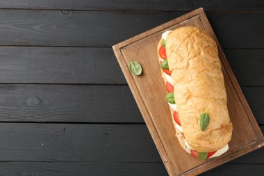 Mozarella peynirli, domatesli, fesleğenli, siyah ahşap masa manzaralı lezzetli bir sandviç. Metin için boşluk